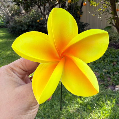 A bright yellow artificial plumeria flower with orange gradients at the petal tips